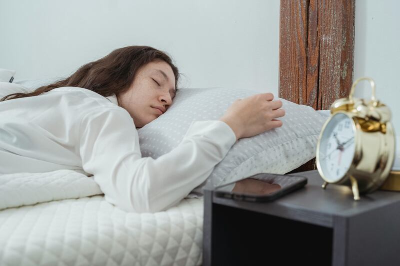 Mulher dormindo ao lado de despertador e celular