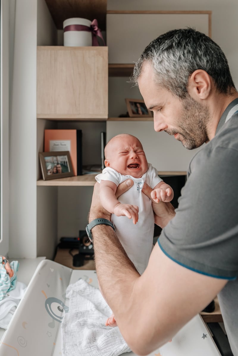 Padre blanco aguantando a su bebe mientras llora.